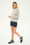 A person stands wearing a light gray sweatshirt, SPLITS59 Airweight High Waist Short in Indigo perfect for hot yoga, and dark athletic shoes.