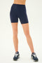 Person wearing SPLITS59 Airweight High Waist Short in Indigo and black running shoes stands against a plain background, ready for a refreshing hot yoga session.