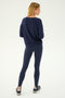 A person stands facing away on a white background, wearing the SPLITS59 Sonja Fleece Sweatshirt in Indigo, paired with matching navy leggings and black sneakers.
