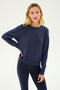A woman stands against a plain background wearing the SPLITS59 Sonja Fleece Sweatshirt in indigo, paired with matching leggings and resting one hand on her hip.