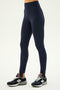 A person wears SPLITS59 River High Waist Airweight Stirrup leggings in Indigo and black New Balance sneakers, perfect for hot yoga, standing against a plain light background.