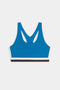 The SPLITS59 Maci Airweight Bra in Stone Blue/Graphite features racerback straps and white and black trim along the bottom band, shown against a plain white background.