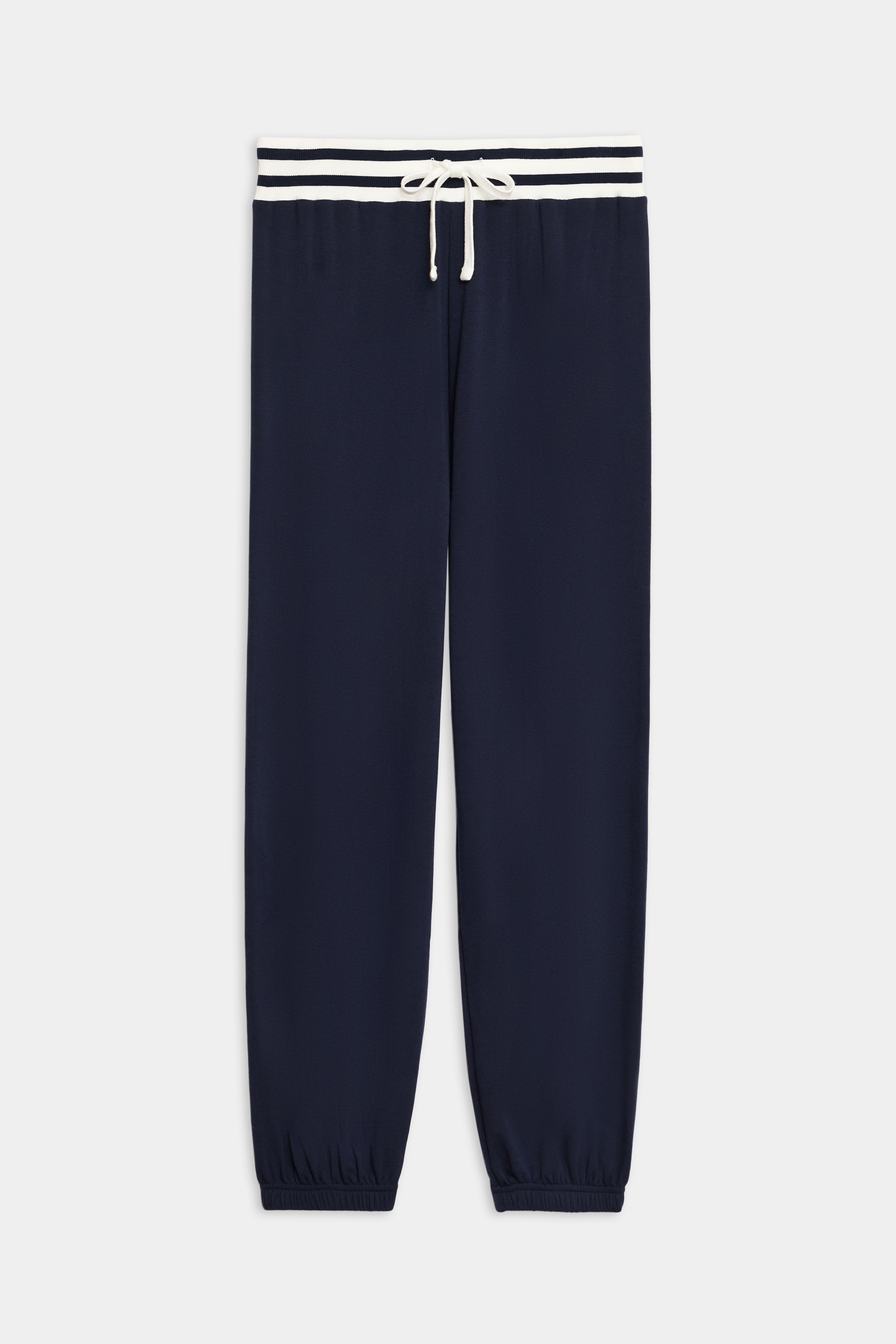 The Andie Oversized Fleece Sweatpant with Stripe by SPLITS59 features navy blue fabric, elasticated cuffs, a white drawstring, and a white waistband accented by two navy stripes.