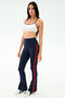 A woman faces forward in the SPLITS59 Loren Seamless Bra in White/Indigo with navy leggings featuring red side stripes and white sneakers—ideal for yoga or gym sessions—set against a plain white background.