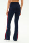 A person is seen from the back wearing SPLITS59 Raquel High Waist Supplex Flare leggings in Indigo/Lotus Red, featuring a navy high-waisted, flared silhouette with red side stripes and 4-way stretch, against a plain white background.