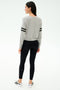 A woman stands facing away, wearing the SPLITS59 Brooks Stripe Fleece Sweatshirt in Heather Grey/Black, paired with black leggings and white sneakers, set against a plain white background.