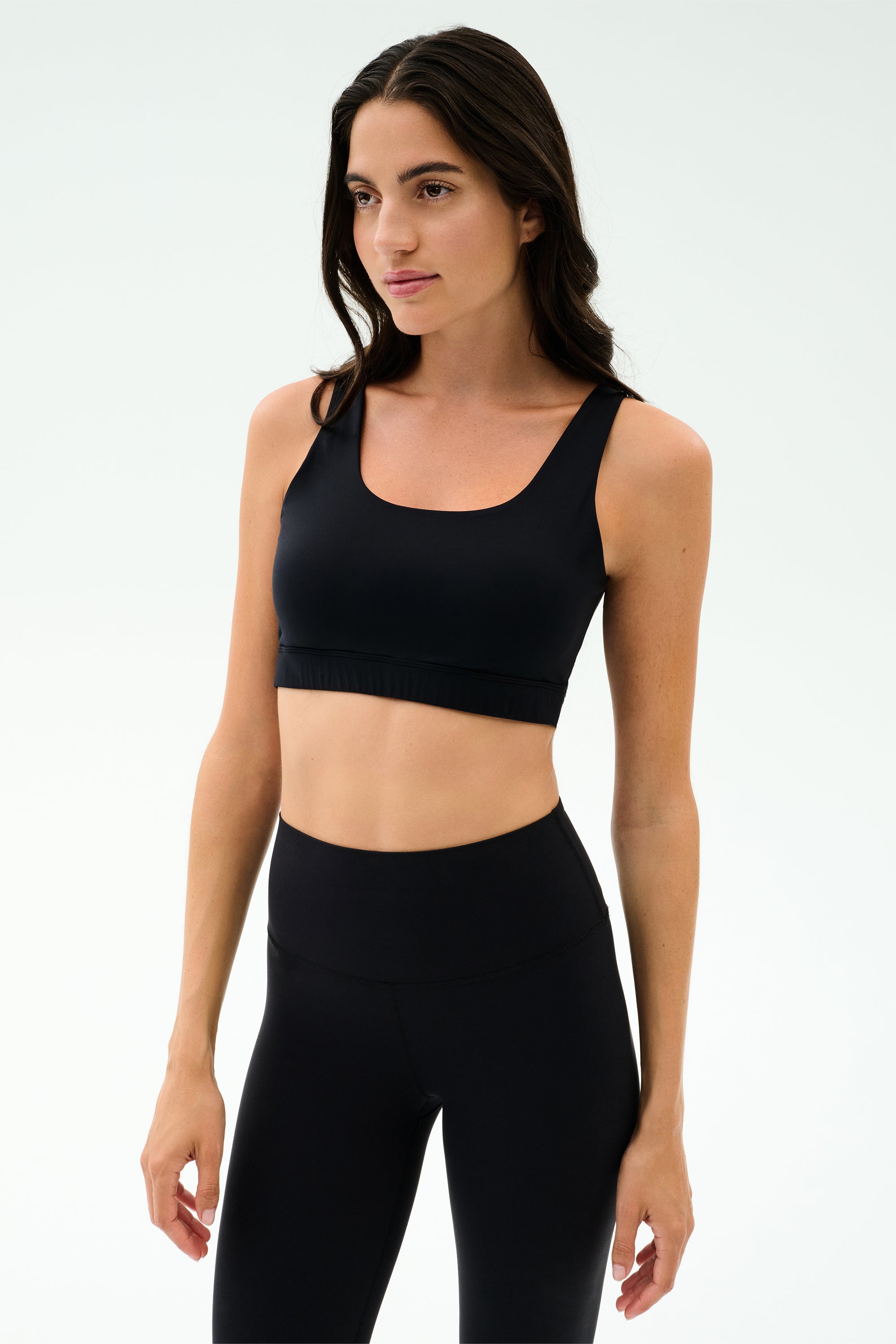 A woman wears the SPLITS59 Sprint Rigor Bra in black, paired with high-waisted leggings, standing against a light background—ready for gym workouts or multisport performance.