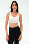 A woman wears the SPLITS59 Sprint Rigor Bra - White with black high-waisted leggings, standing against a plain white background, ready for gym workouts and multisport performance.