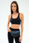 A woman stands against a white background wearing a black sports bra, black leggings with blue stripes, and the SPLITS59 MZW x Splits59 Small Metro Sling.