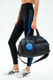Wearing black leggings with blue stripes and white sneakers, a person carries the SPLITS59 MZW x Splits59 Duffle—a quilted black bag with blue accents and a round blue and red keychain.