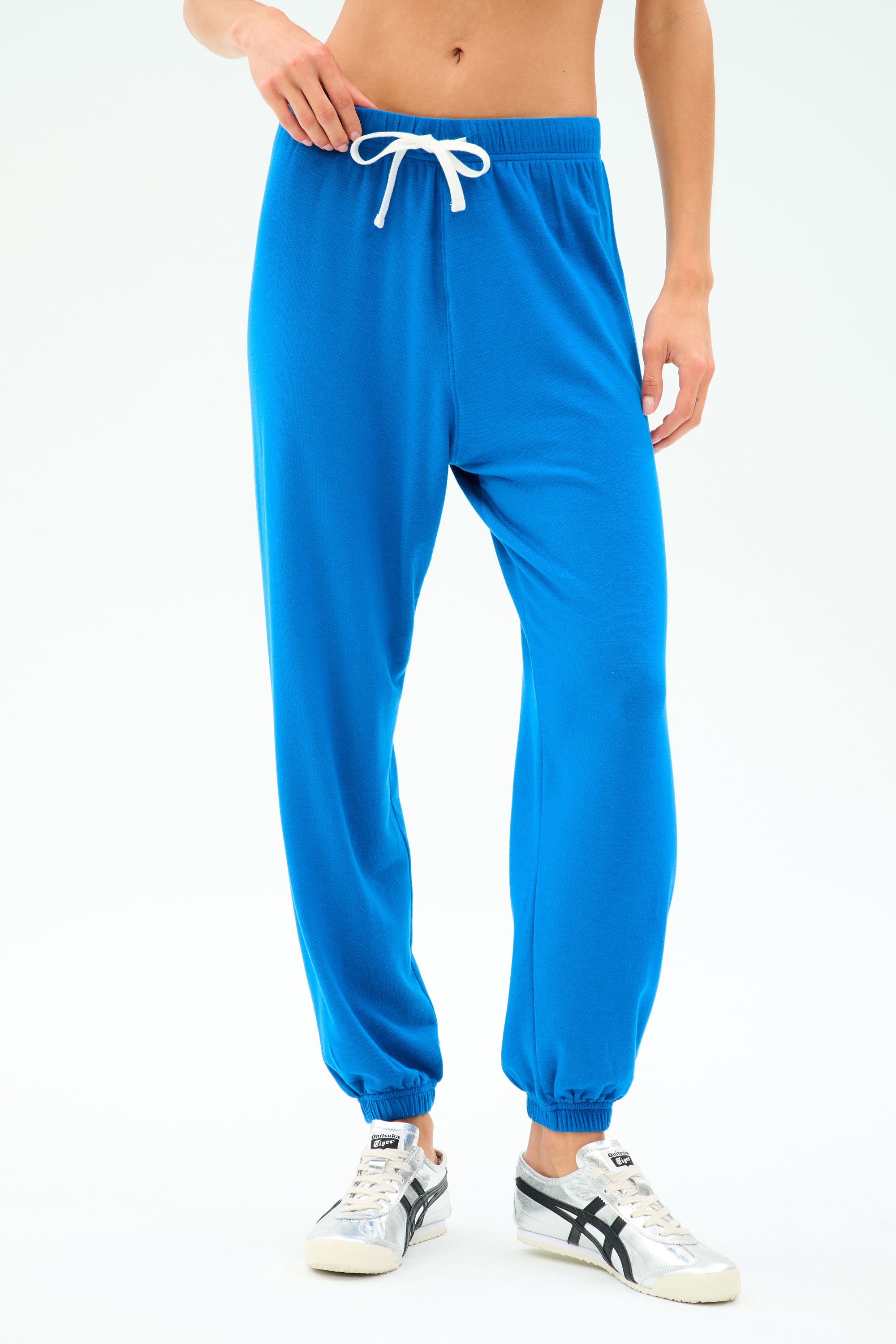 Model wearing SPLITS59 Andie Oversized Fleece Sweatpant in Classic Blue with white drawstring and white sneakers, posed against a plain light background.