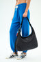 A person in blue jogger pants and white sneakers carries the SPLITS59 MZW x Splits59 Carry All, a large black quilted shoulder bag with a strap and small decorative keychains.