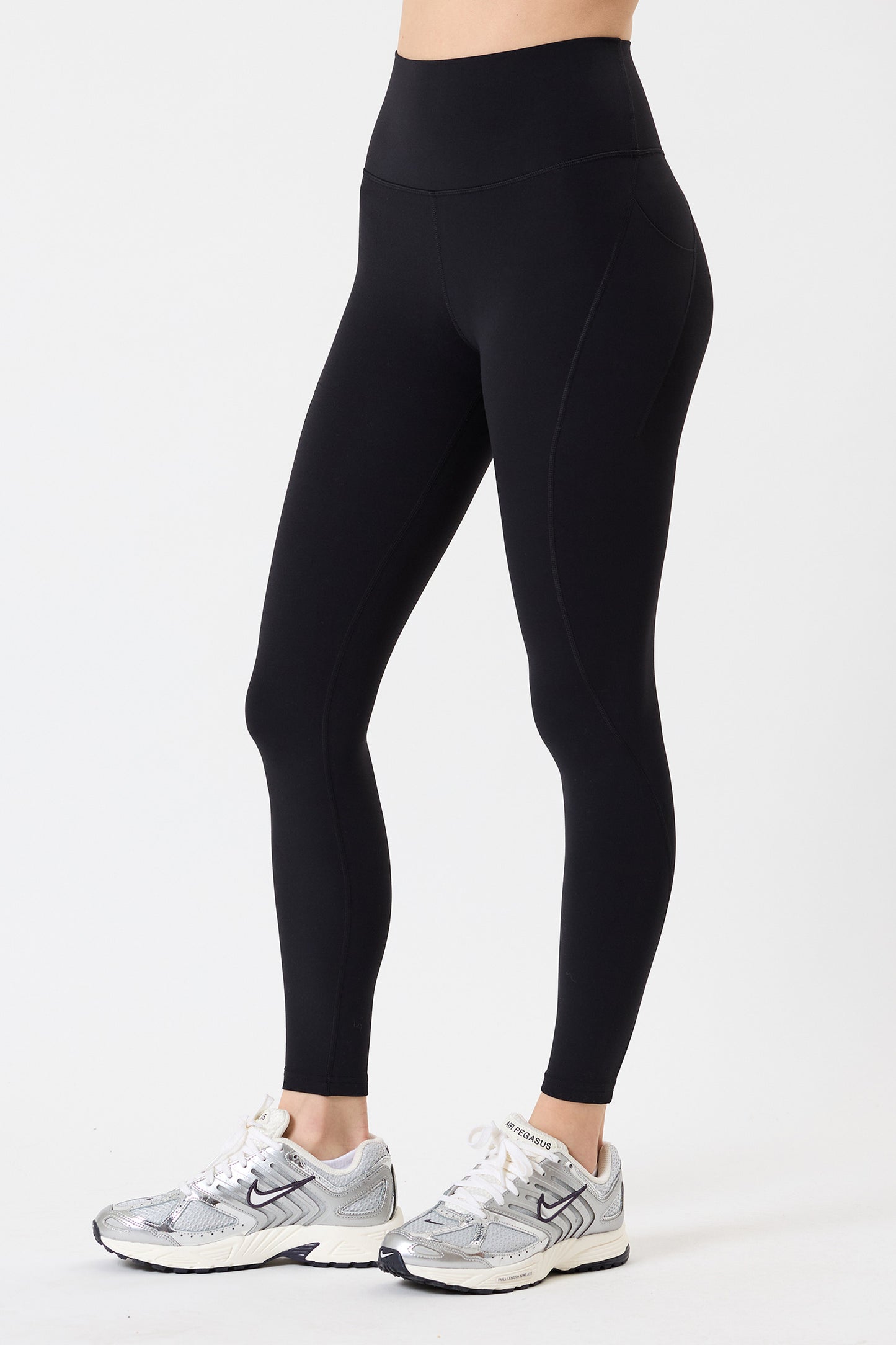 A person in SPLITS59 Airweight High Waist 7/8 Pocket Legging in Black with silver athletic shoes stands against a plain white background. These ultra luxe leggings are perfect for hot yoga sessions.