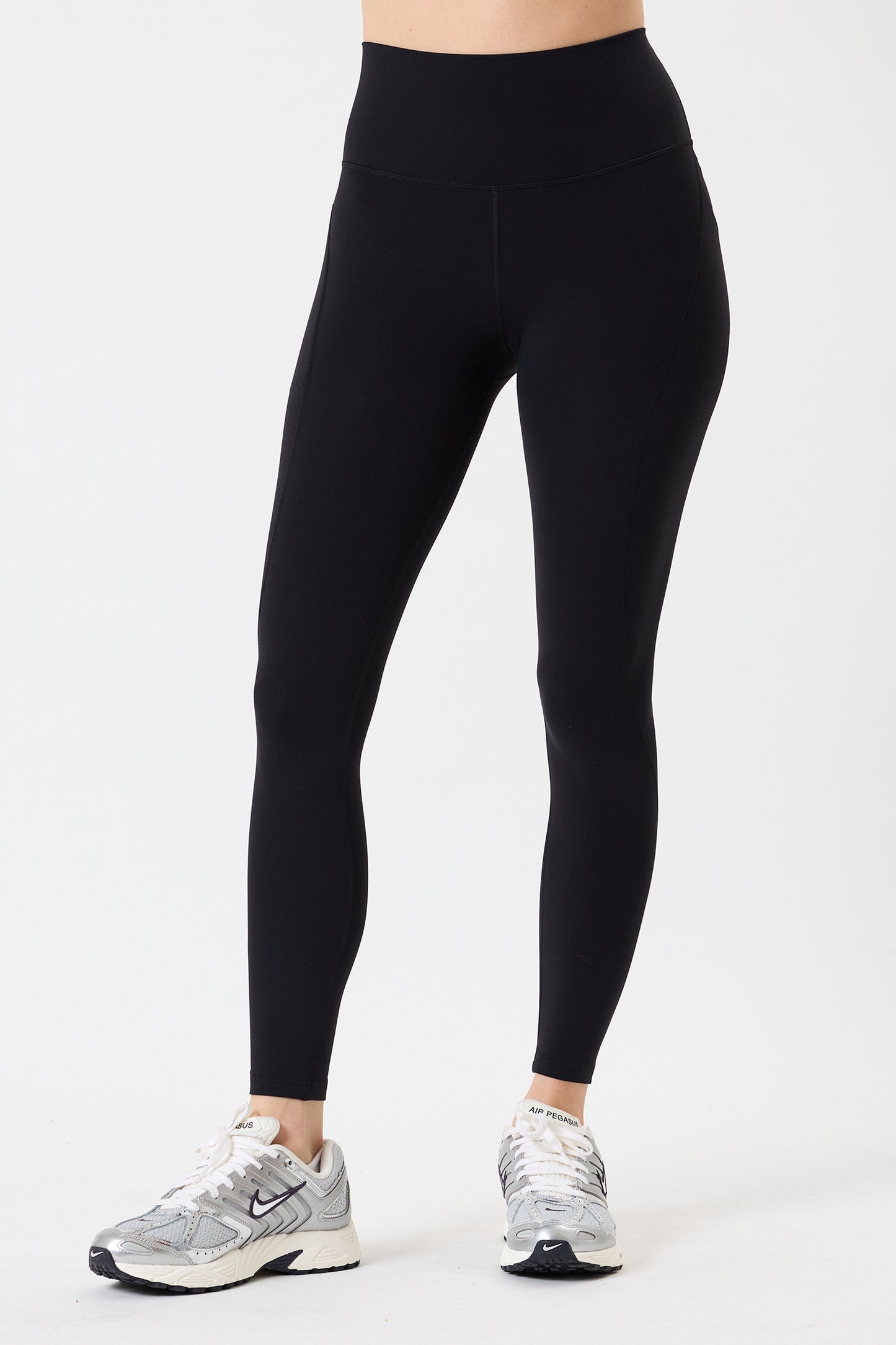 A person wears SPLITS59 Airweight High Waist 7/8 Pocket Legging in black and white athletic shoes, standing against a plain white background.