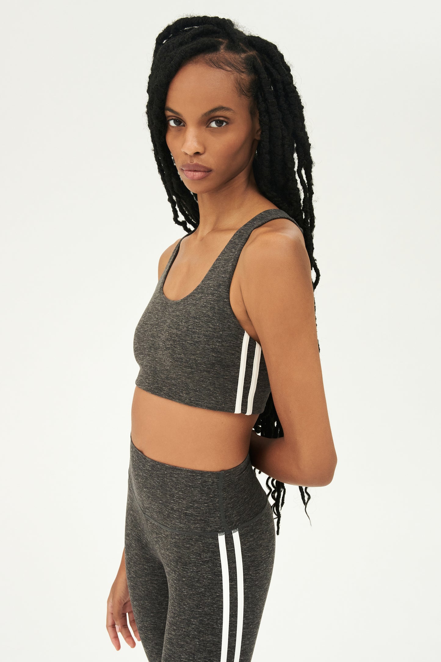 Side view of girl wearing light dark grey sports bra with two thin white stripes down the side and light dark grey leggings