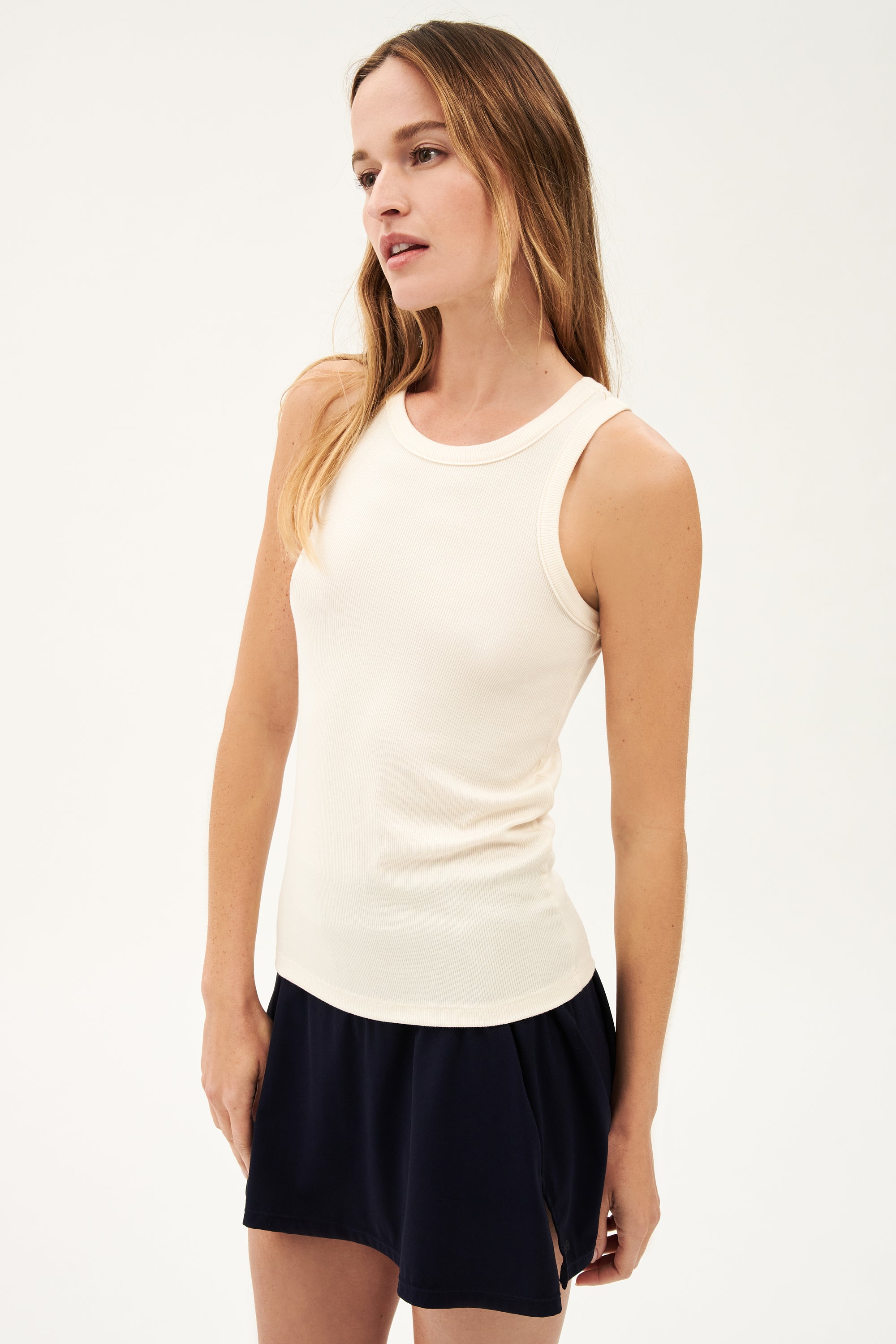 A woman in a Kiki Rib Tank Full Length - Creme by SPLITS59 and black skirt, doing yoga.