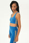 Side view of girl wearing blue sports bra with two thin yellow stripes down the side and blue leggings