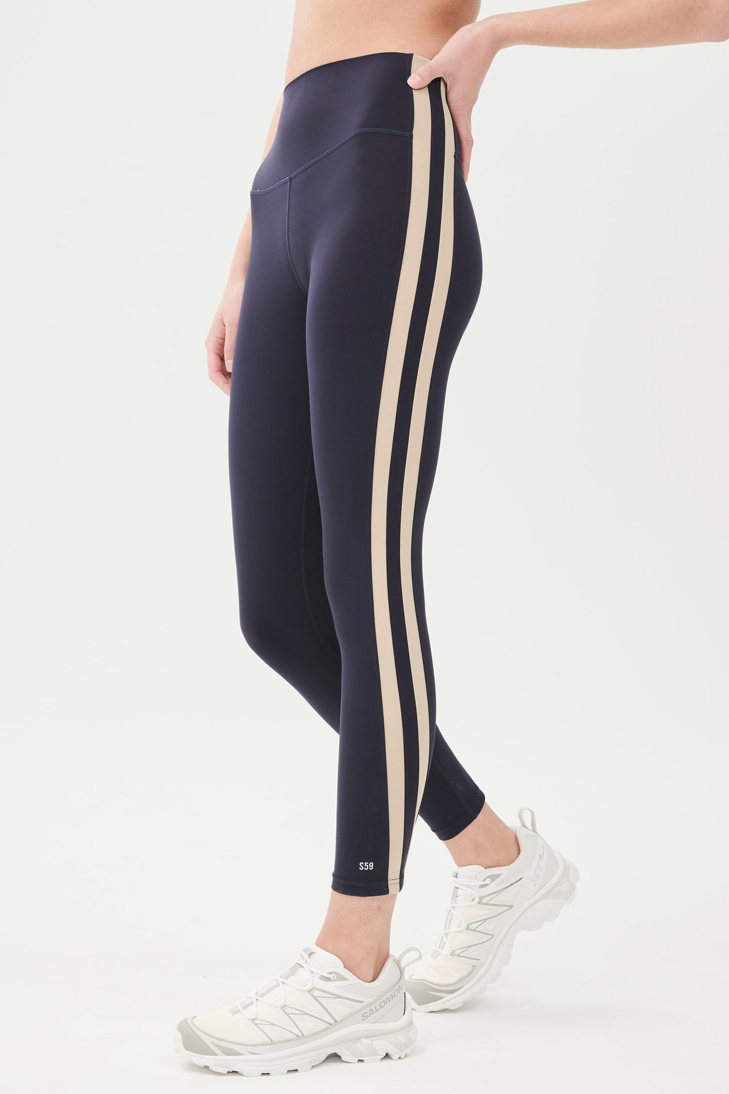 Side view of girl wearing a dark blue leggings with light brown colored stripe down the side and white shoes