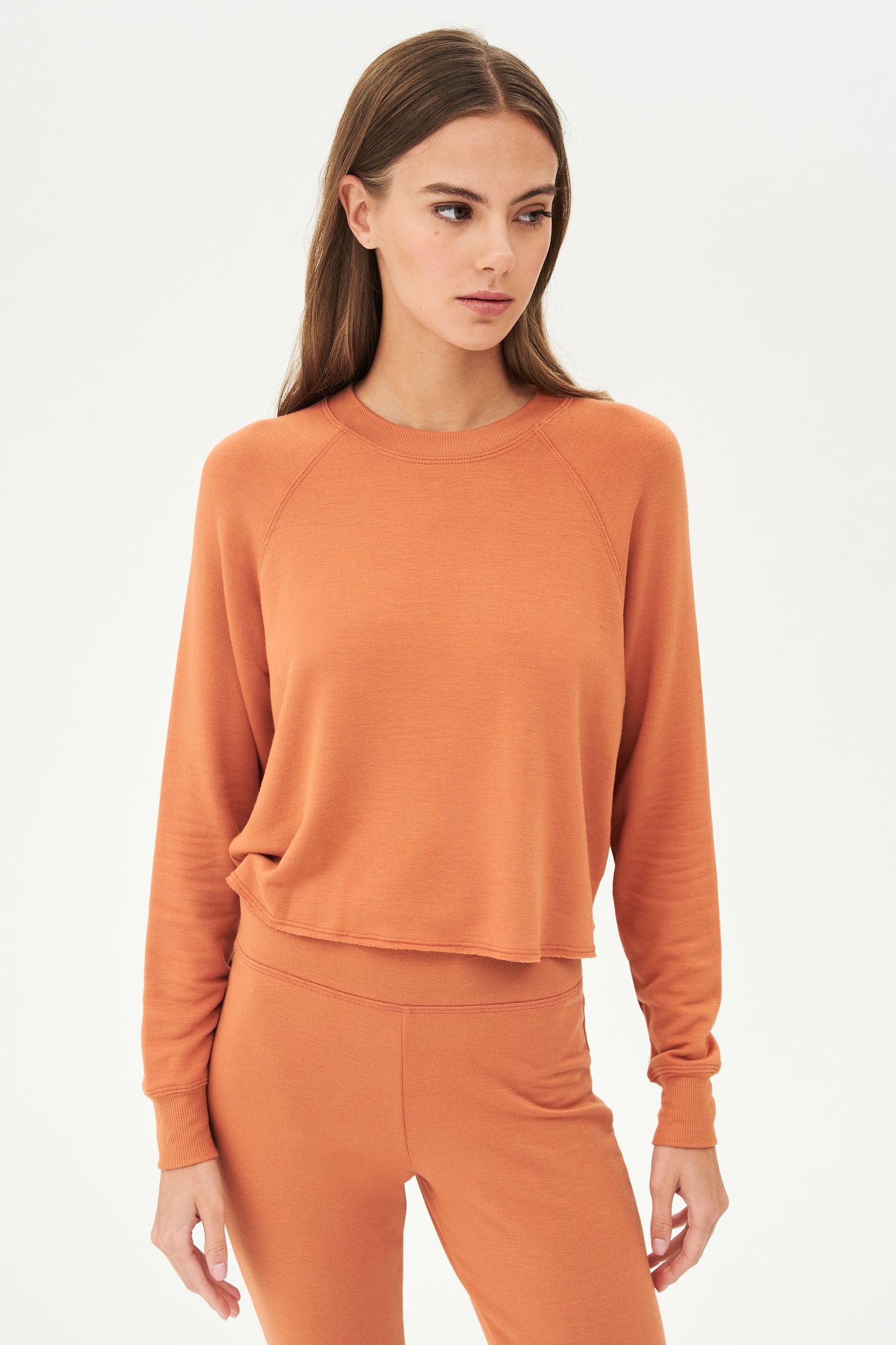 Front view of woman with brown hair wearing orange cropped sweatshirt and orange leggings