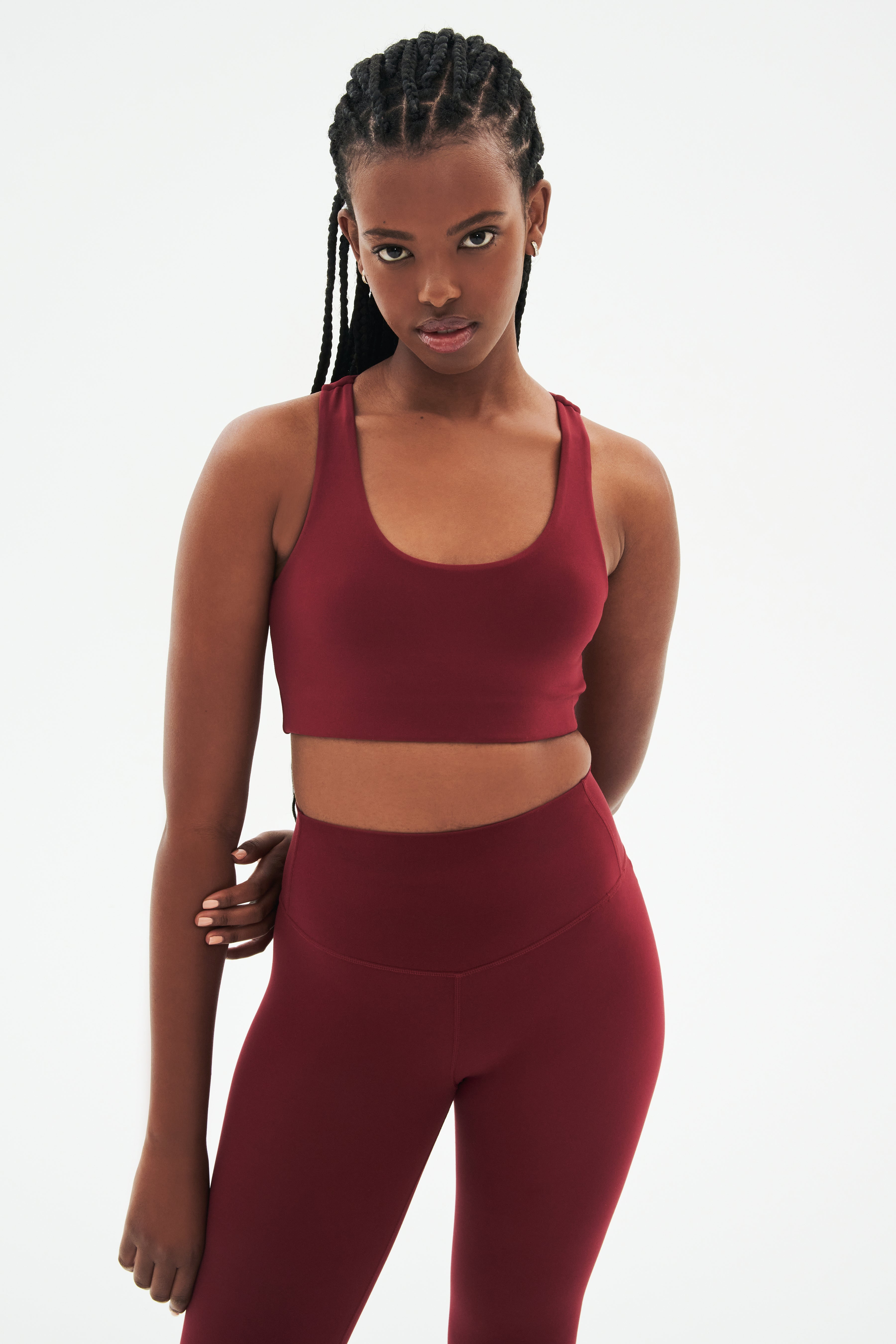 Front view of woman with black braids wearing dark red bra and dark red leggings