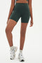 Front view of girl wearing highwaisted mid thigh dark dark green bike shorts with white shoes