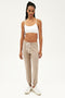 Full front view of woman with black braids wearing light earthy brown sweatpant jogger with white drawstring and white bra with spaghetti straps paired with white shoes