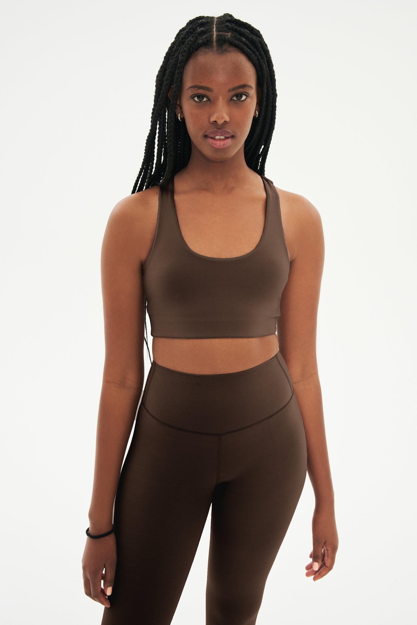 Front view of woman with black braids wearing dark brown bra and dark brown leggings