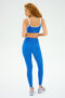 A person with curly hair wears a SPLITS59 blue workout set, showcasing the Cait Rigor Bra in Classic Blue/White, viewed from the back against a plain background.