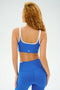 A curly-haired individual, wearing the SPLITS59 Cait Rigor Bra in Classic Blue/White, prepares for high-performance workouts.
