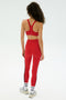 A person faces away on a white background, wearing the SPLITS59 Ella Airweight Bra in red with matching side-striped leggings, white socks, and silver sneakers.