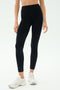 A person in SPLITS59 Emerson Airweight High Waist leggings in Black/Ice and white sneakers stands against a plain light background, ready for Pilates or hot yoga.