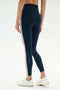 A person shown from the back wears SPLITS59 Margot Rigor Legging in Indigo/Blush, featuring pink and white side stripes, paired with white athletic shoes against a plain background.