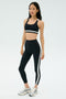 On a white background, a person wears the SPLITS59 Miles Rigor Bra - Black/White with matching striped leggings and silver athletic shoes—ideal for gym workouts and optimal support.