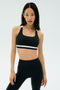 A woman wears the SPLITS59 Miles Rigor Bra - Black/White with black leggings, standing against a light background, ready for her workout.