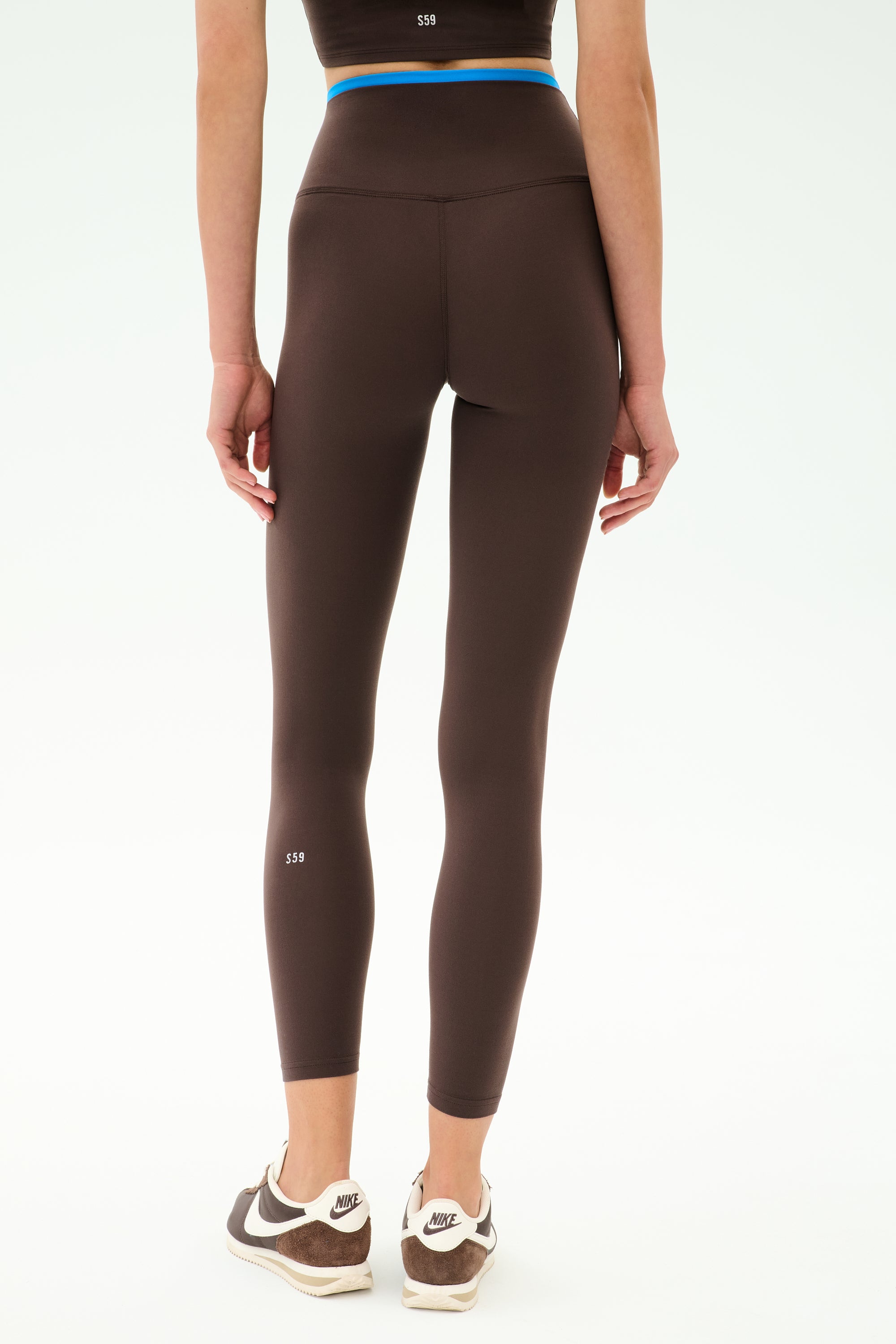 Person standing in SPLITS59 Dual High Waist Airweight 7/8 leggings in Dark Chocolate/Classic Blue and black-and-white Nike sneakers, viewed from the back against a plain white background.