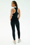 A person faces away, wearing the SPLITS59 Amber Airweight High Waist 7/8 Black/White leggings with a matching sleeveless top and white sneakers, set against a plain light background.