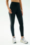 A person wears SPLITS59 Amber Airweight High Waist 7/8 leggings in black/white with white athletic shoes, standing against a plain background.