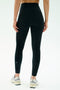 A person faces away, wearing SPLITS59's Amber Airweight High Waist 7/8 leggings in Black/White and light sneakers, set against a plain, light background.