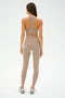 A woman in ultra-luxe beige sportswear and sneakers, featuring the SPLITS59 Sara Airweight Bra in Latte, stands with her back to the camera against a plain background.