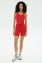 A woman stands against a plain background wearing SPLITS59's Ella High Waist Airweight Short in Pirate Red/Indigo, paired with a red tank top, white socks, and white sneakers.
