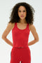 A person with curly hair wears the SPLITS59 Ashby Rib Crop in Pirate Red, paired with matching leggings and stands against a plain white background, looking straight ahead with hands behind their back—ready for the gym.