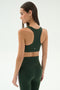 A woman models the SPLITS59 Lexi Rigor Bra in Military/Blush, paired with high-waisted leggings, standing with her back to the camera against a plain light background.