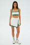 Someone is dressed in an SPLITS59 Monah Rigor Skort in White/Arugula, which includes a sports bra and skirt, against a plain background.