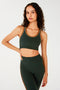 Front view of woman with dark wavy hair wearing dark green bra with white and dark orange border arm and neckline and dark green leggings with dark orange double side stripes.