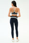 A woman faces away, wearing the SPLITS59 Emerson Airweight Bra in Indigo/Dove Grey with matching high-waisted leggings and white sneakers—ideal for hot yoga—set against a plain background.