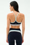 A woman faces away, wearing the SPLITS59 Emerson Airweight Bra in Indigo/Dove Grey with matching high-waisted leggings—ideal for hot yoga—set against a plain, light background.