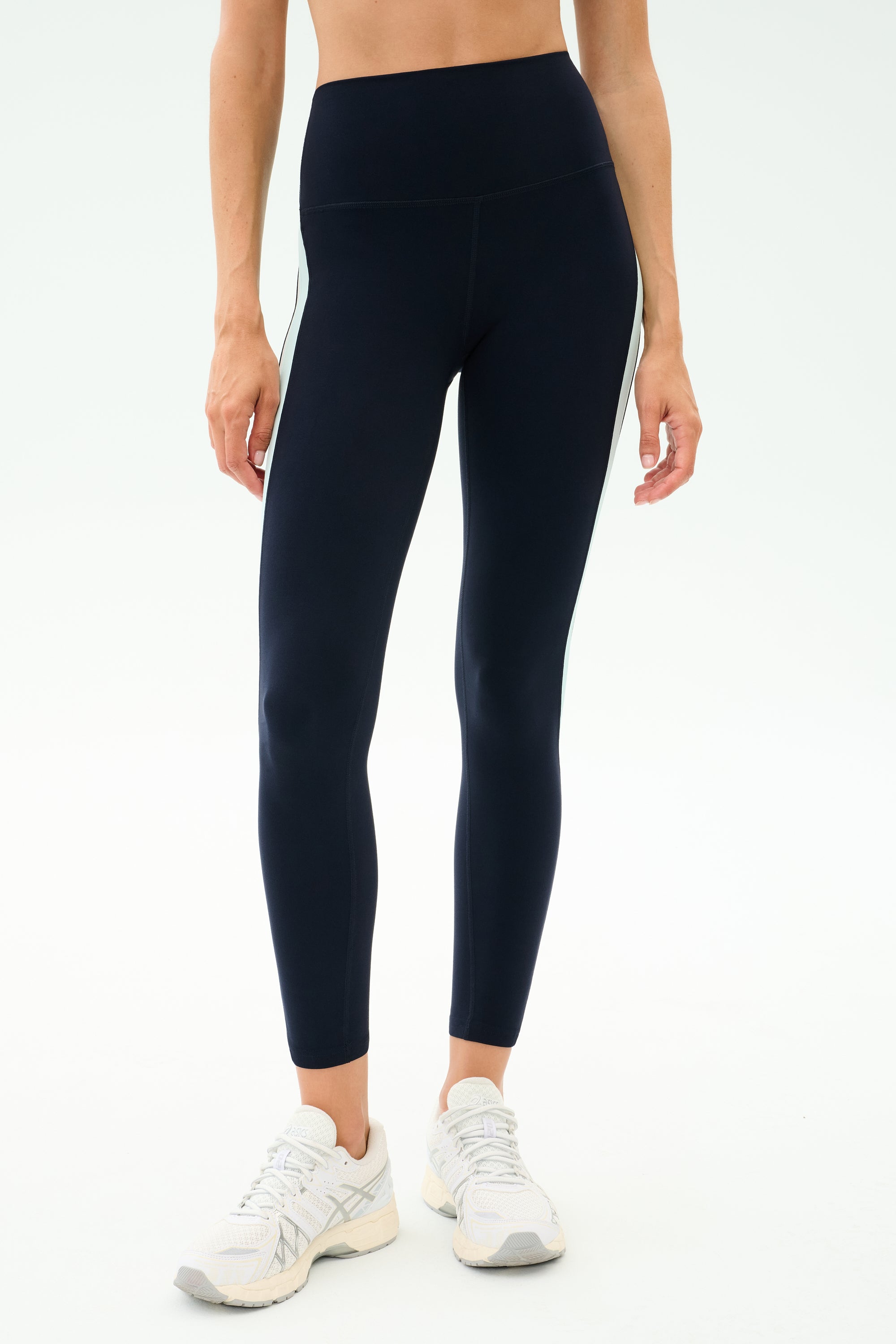Person wearing SPLITS59 Emerson Airweight High Waist leggings in Indigo/Dove Grey and white sneakers, standing against a plain light background—ideal for Pilates or hot yoga sessions.