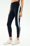 A person wears SPLITS59 Emerson Airweight High Waist leggings in Indigo/Dove Grey—navy with a vertical light blue and white stripe—ideal for Pilates, paired with white athletic shoes, standing against a plain background.