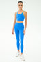 A person wears the SPLITS59 Amber Airweight Bralette in Classic Blue/Ray with matching leggings and white sneakers, standing against a plain white background.