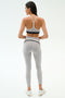 A woman in the SPLITS59 Emerson Airweight High Waist leggings in Dove Grey/Indigo and a sports bra stands facing away on a plain white background, highlighting a sculpted silhouette.